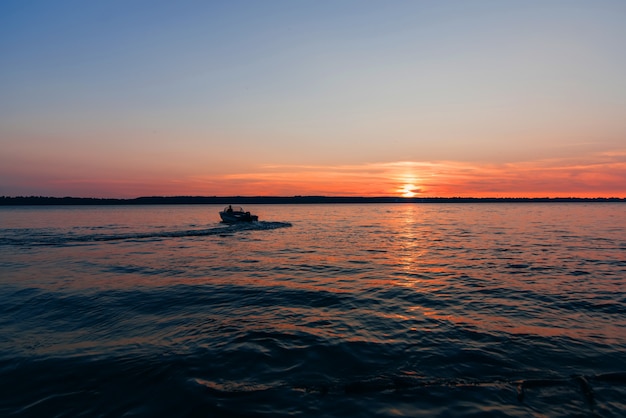 太陽と赤と青の夕日の背景に水の波に浮かぶボート