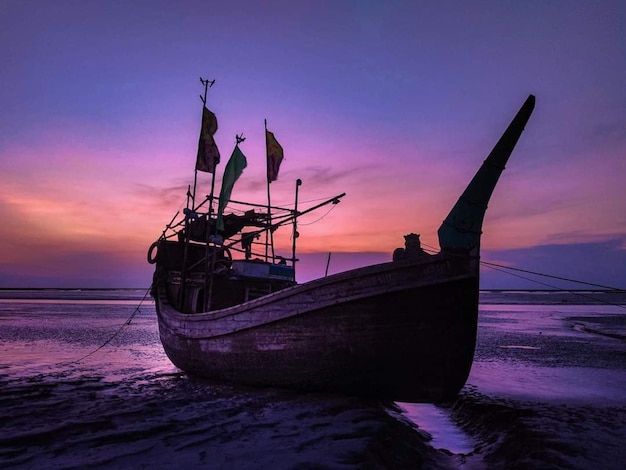 A boat is docked at a beach with a purple sky in the background.