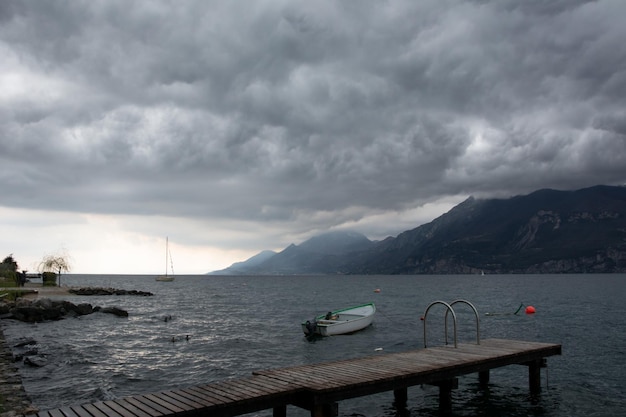 A boat is moored near a sea wooden pier on a cloudy day with dark clouds High mountains