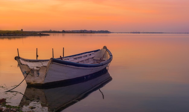 boat moored on calm lake against sky during sunset