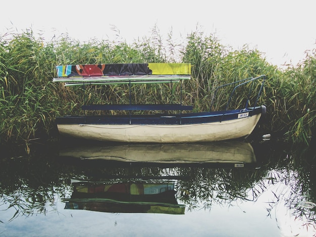 Photo boat moored on calm river by plants against clear sky