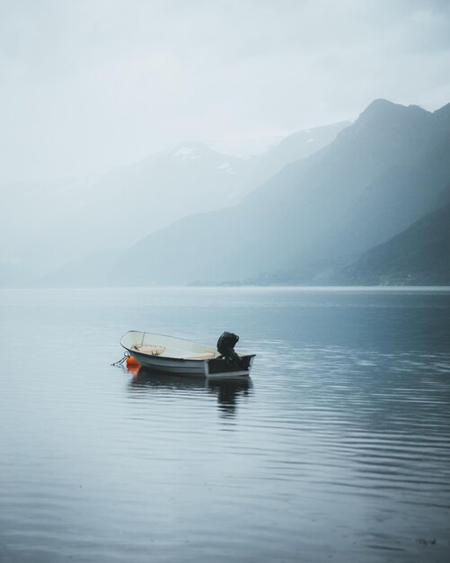 Boat moored on lake against mountains during foggy weather