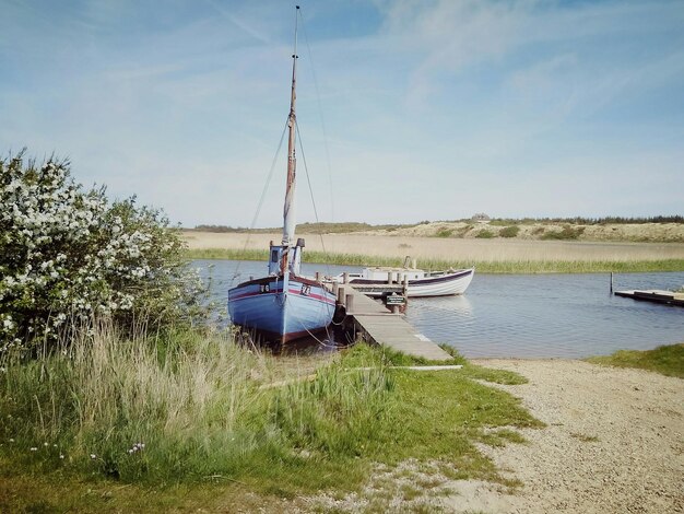 Boat moored on river by field against sky