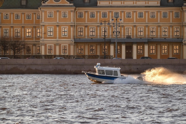 A boat rides with splashes along the river against the background of a historical building on the em