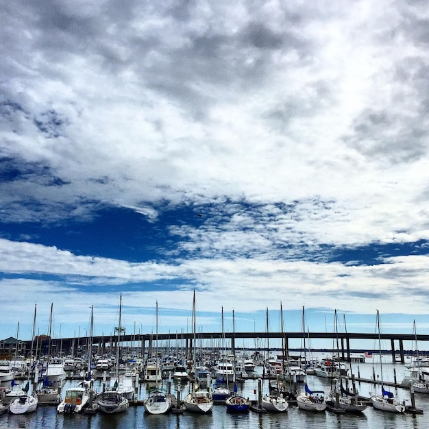 Boats in harbor against cloudy sky