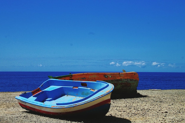 Boats moored at beach against blue sky