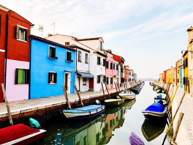 Boats moored in canal by houses against sky