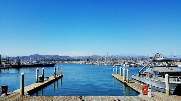 Boats moored at harbor against clear blue sky