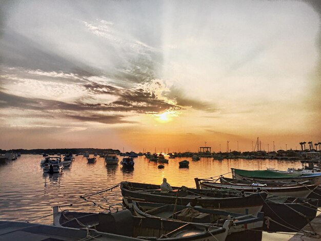 Photo boats moored at harbor during sunset