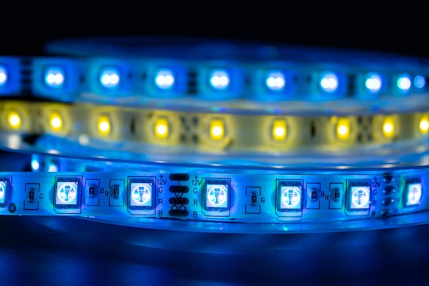 Bobbin with roll of glowing LED strip lighting placed on table blue and warm white color