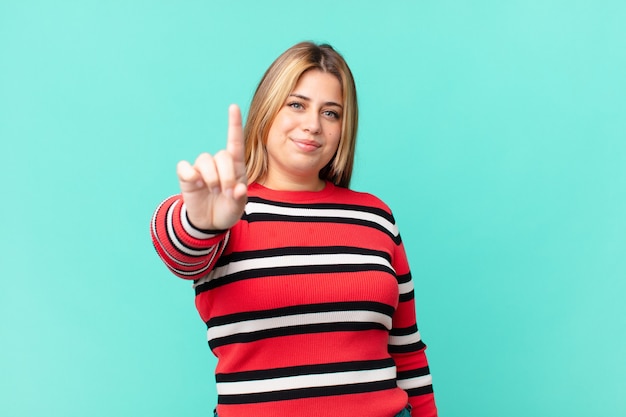 Bochtige mooie blonde vrouw die lacht en er vriendelijk uitziet, met nummer één