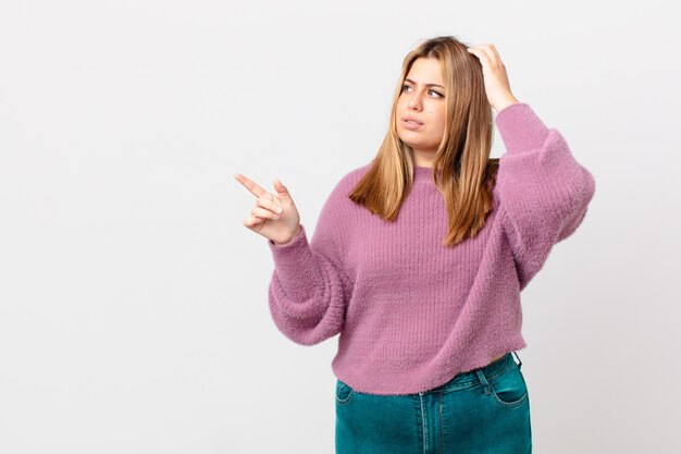 Bochtige, mooie blonde vrouw die zich verbaasd en verward voelt en haar hoofd krabt