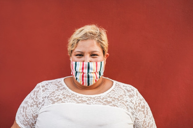 Bochtige vrouw die op camera glimlacht terwijl het dragen van een beschermend gezichtsmasker buiten - coronavirus-levensstijlconcept