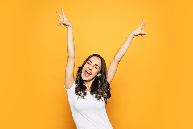 Bodacious awake girl with her hands up showing Ã¢ÂÂpeaceÃ¢ÂÂ sign, wide smile and the tongue out of the mouth which tells about her happy mood