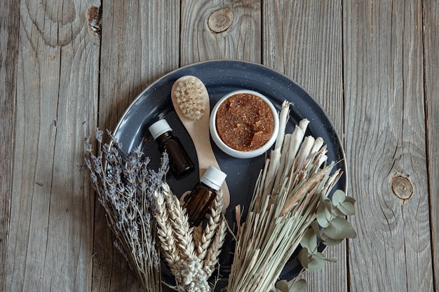 Body brush, natural scrub, oils and a bouquet of field herbs on a wooden surface.