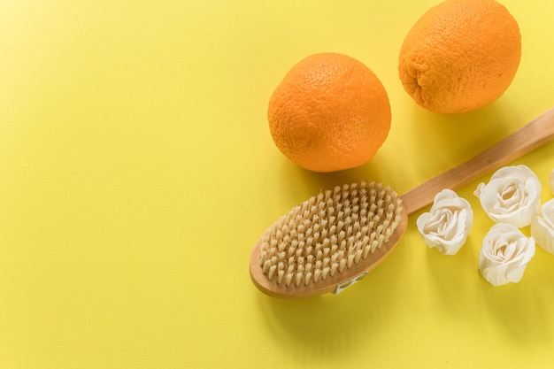 Body brush with big oranges and white soap in rose form for anti-cellulite massage on yellow wall. Flat lay design with copy space. Cactus exfoliating brush for body care