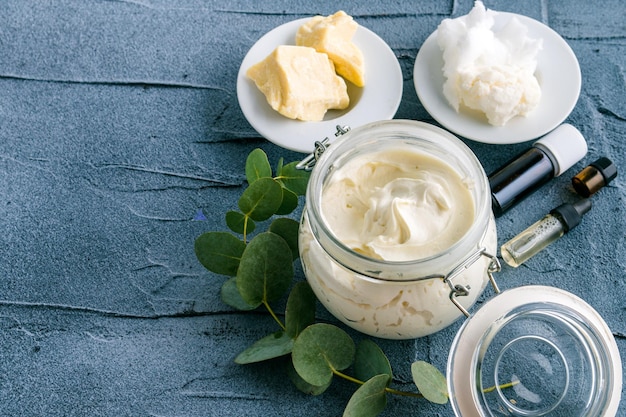 body butter with ingredients and essential oil on a dark concrete background