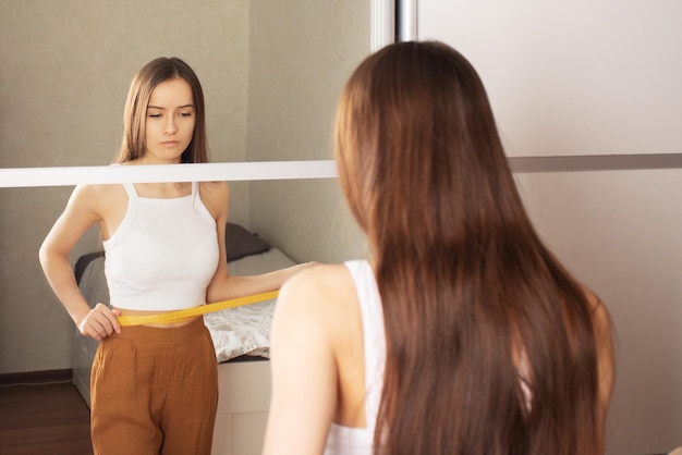 Body care beauty healthy eating teen girl in front of the mirror measures her waist with a ribbon