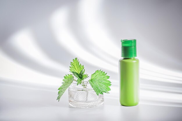 Body cream or lotion with nettle leavesin a plastic container on a white background with trendy shadows