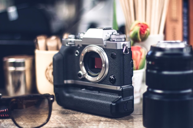 Corpo della fotocamera digitale sul tavolo e altre cose intorno, come obiettivo, occhiali da sole, tazze e fiori.