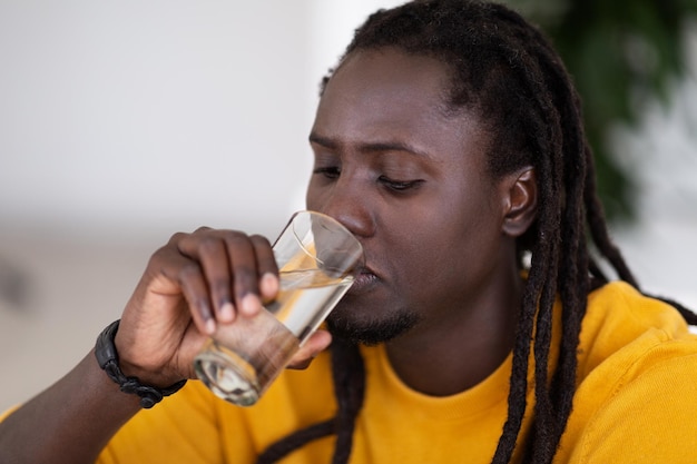 Гидратация тела Молодой черный мужчина с дредами пьет воду из стекла