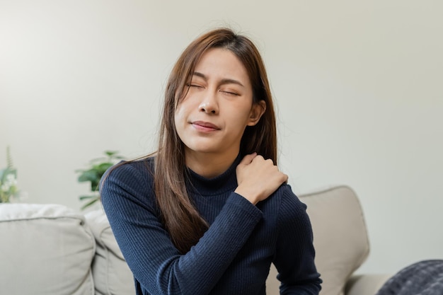Body muscles stiff problem asian young attractive woman girl\
pain with back pain ache from work holding massaging rubbing\
shoulder hurt or sore painful sitting on sofa at home healthcare\
people