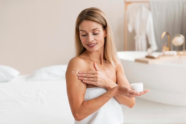 Foto trattamenti per il corpo felice donna di mezza età che applica crema idratante sulla spalla facendo routine di bellezza