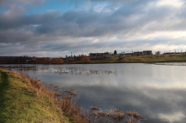 A body of water with grass and a cloudy sky