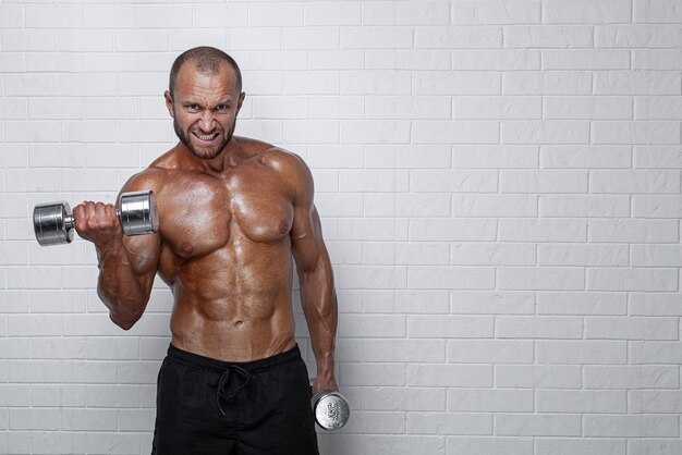 Bodybuilder doing exercises for biceps with a dumbbells against brick wall.