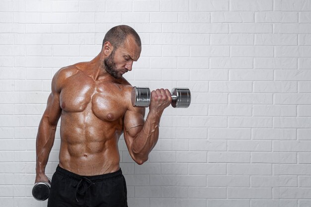 Bodybuilder doing exercises for biceps with a dumbbells against brick wall.