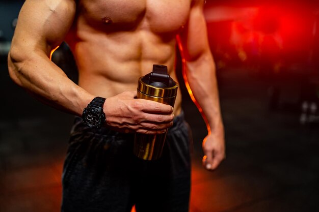 Bodybuilder is posing with sport cup in hands Beautiful sporty guy male power Fitness muscled man without shirt on dark gym background