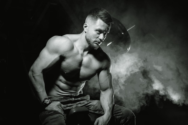 Bodybuilder in posa su sfondo nero seduto su una panchina dopo l'allenamento uomo muscolare in palestra foto in bianco e nero