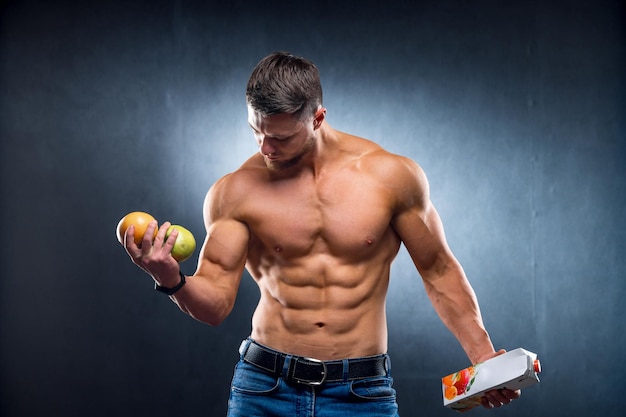 Bodybuilder sportman met fruit en sap Kiezen tussen pure of geconcentreerde drank Portret Grijze achtergrond Close-up