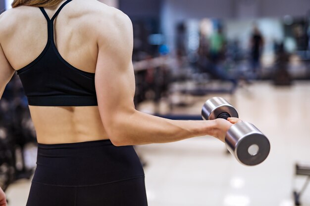 Bodybuilderwijfje die in sportkleding achteruitgaan die wapen en rugspieren met domoor in de fitness club oppompen.