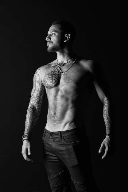 Cura del corpo con fitness e sport uomo tatuato mostra torso muscoloso sexy sportivo con confezione da sei e ab bodybuilder con bicipiti e tricipiti modello di moda con tatuaggio in jeans