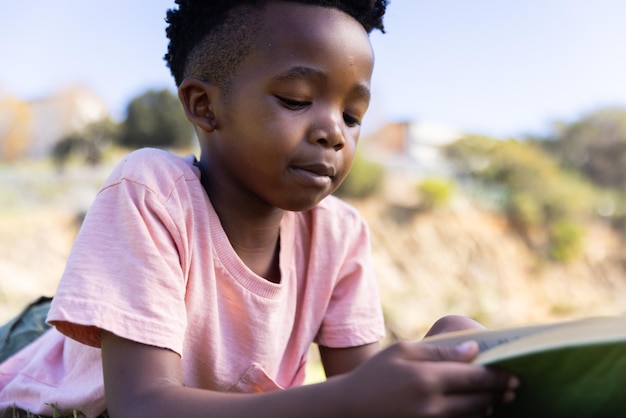 Boek lezen buiten jonge Afro-Amerikaanse jongen die zich concentreert op het verhaal genieten van de natuur