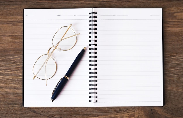 Boek voor notitie, bril en pen geplaatst op een houten tafel