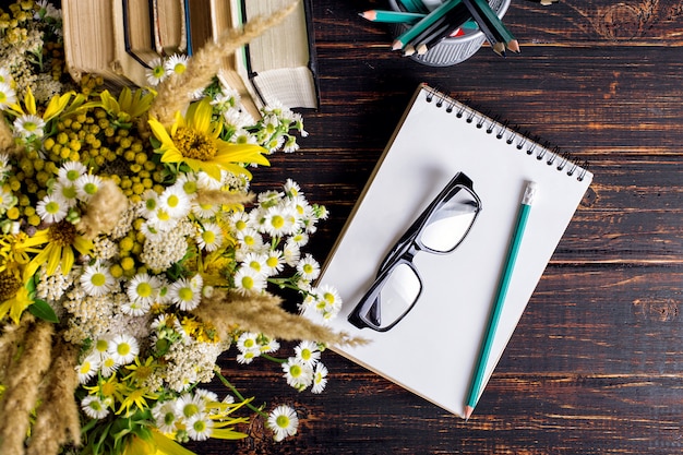 Boeken, glazen, stiften en een boeket bloemen in een vaas op wit