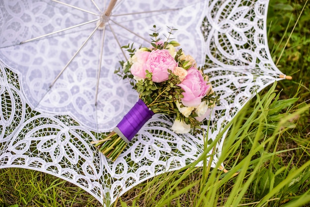 Boeket beige rozen en roze pioenrozen op een witte bruids paraplu in groen gras