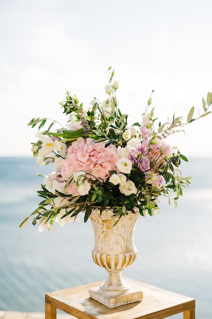 Boeket bloemen in een antieke vaas staat op een krukje tegen de achtergrond van water