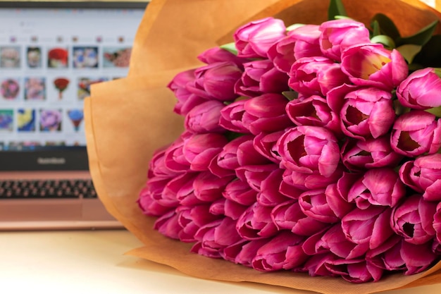 boeket bloemen op tafel tegen de achtergrond van een laptop Het concept van bloemen bestellen