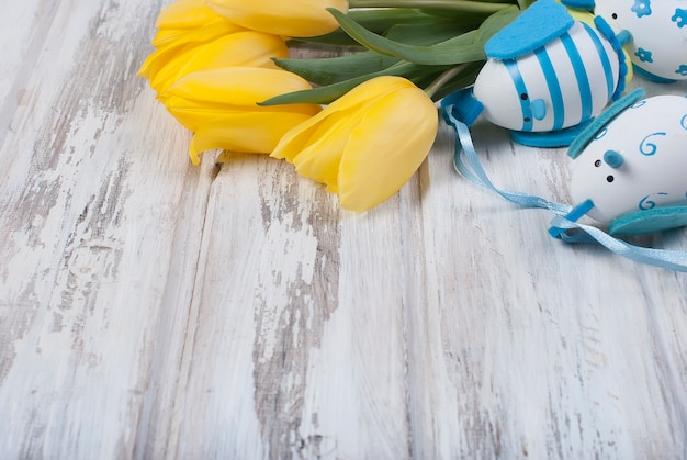 Boeket gele tulpen en chikken paaseieren met een blauw lint op woodenon