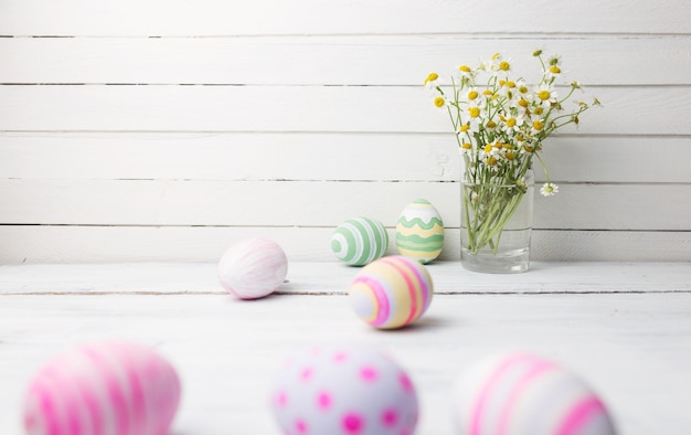 Boeket kamilles in een glazen vaas en paaseieren in pastelkleur op witte vintage planken