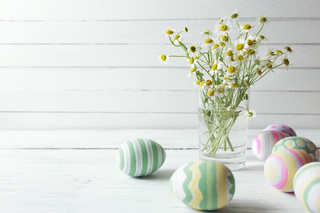 Boeket kamilles in een glazen vaas en paaseieren in pastelkleur op witte vintage planken