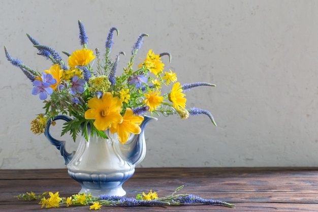 Boeket met blauwe en gele bloemen in theepot op houten tafel