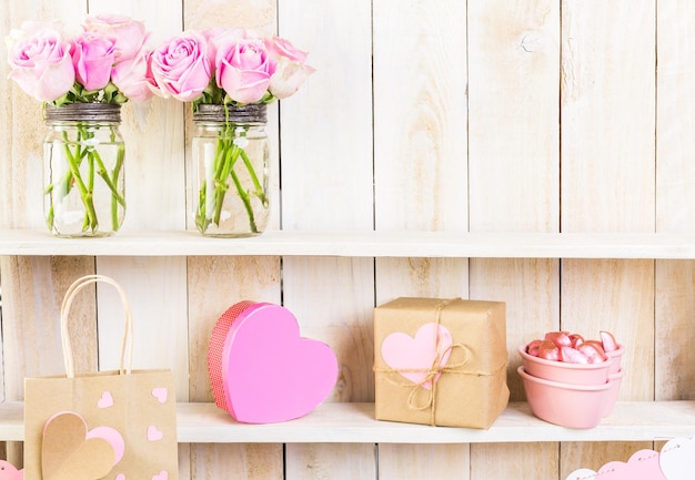 Boeket met roze rozen in stenen pot op houten plank.