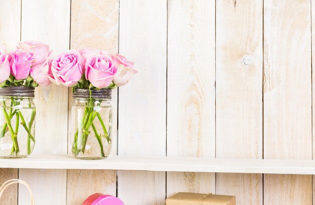 Boeket met roze rozen in stenen pot op houten plank.