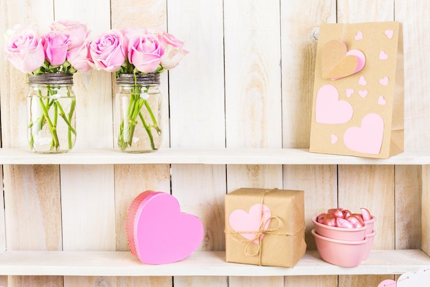 Boeket met roze rozen in stenen pot op houten plank.