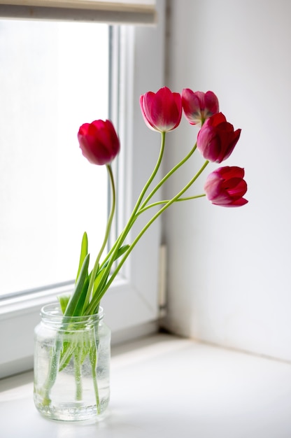 Boeket mooie roze tulpen in een glazen pot op het raam met prachtig licht