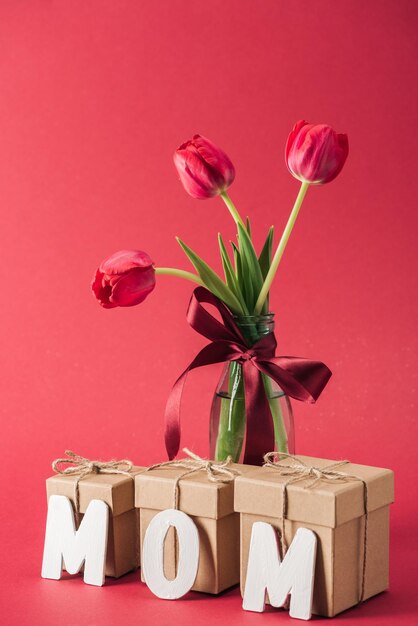 Foto boeket rode tulpen in een glazen vaas en papier woord moeder op rode achtergrond